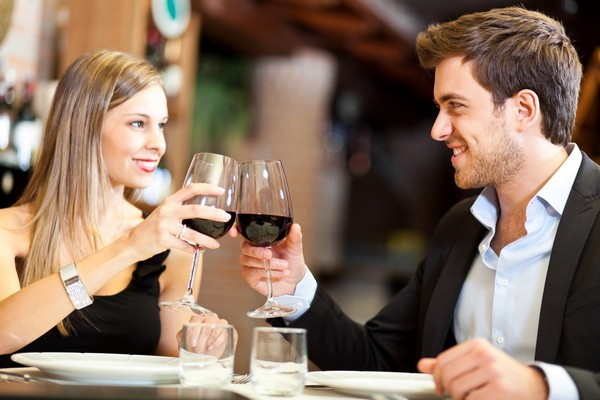 Jeune couple tout souriant trinque au restaurant avec verres de vin rouge 