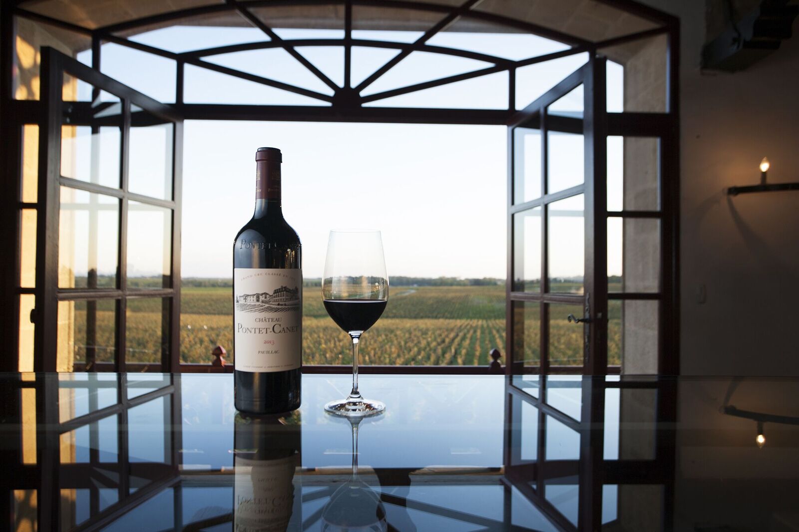Bouteille de vin rouge Pauillac posée sur table, verre vin rouge vue sur vignoble de la fenêtre