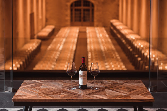 Bouteille de vin rouge avec deux verres à vin, vue sur barriques bordelaises en fond