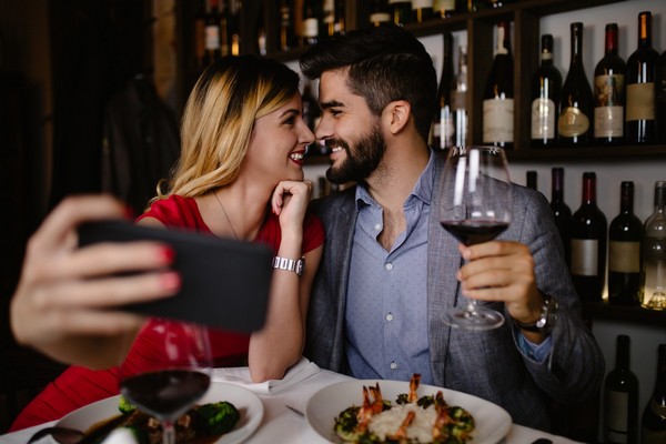 Couple amoureux au restaurant qui tient un verre de vin rouge et fait un selfie