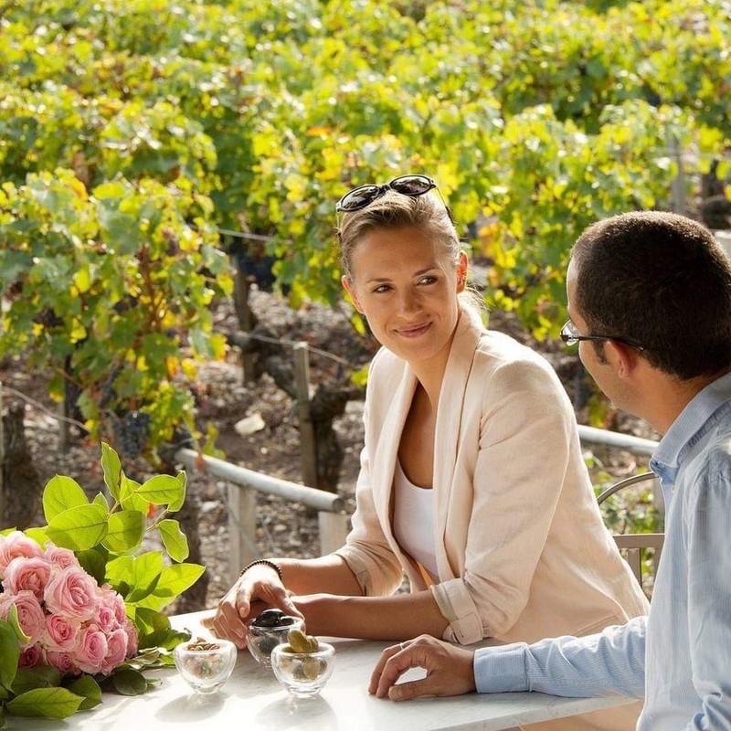 Jeune couple en extérieur sur terrasse, bouquet de roses sur la table, vignoble derrière