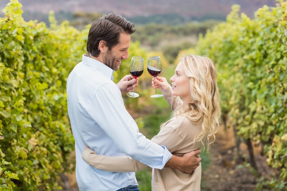 Couple amoureux verre de vin rouge à la main en balade dans le vignoble