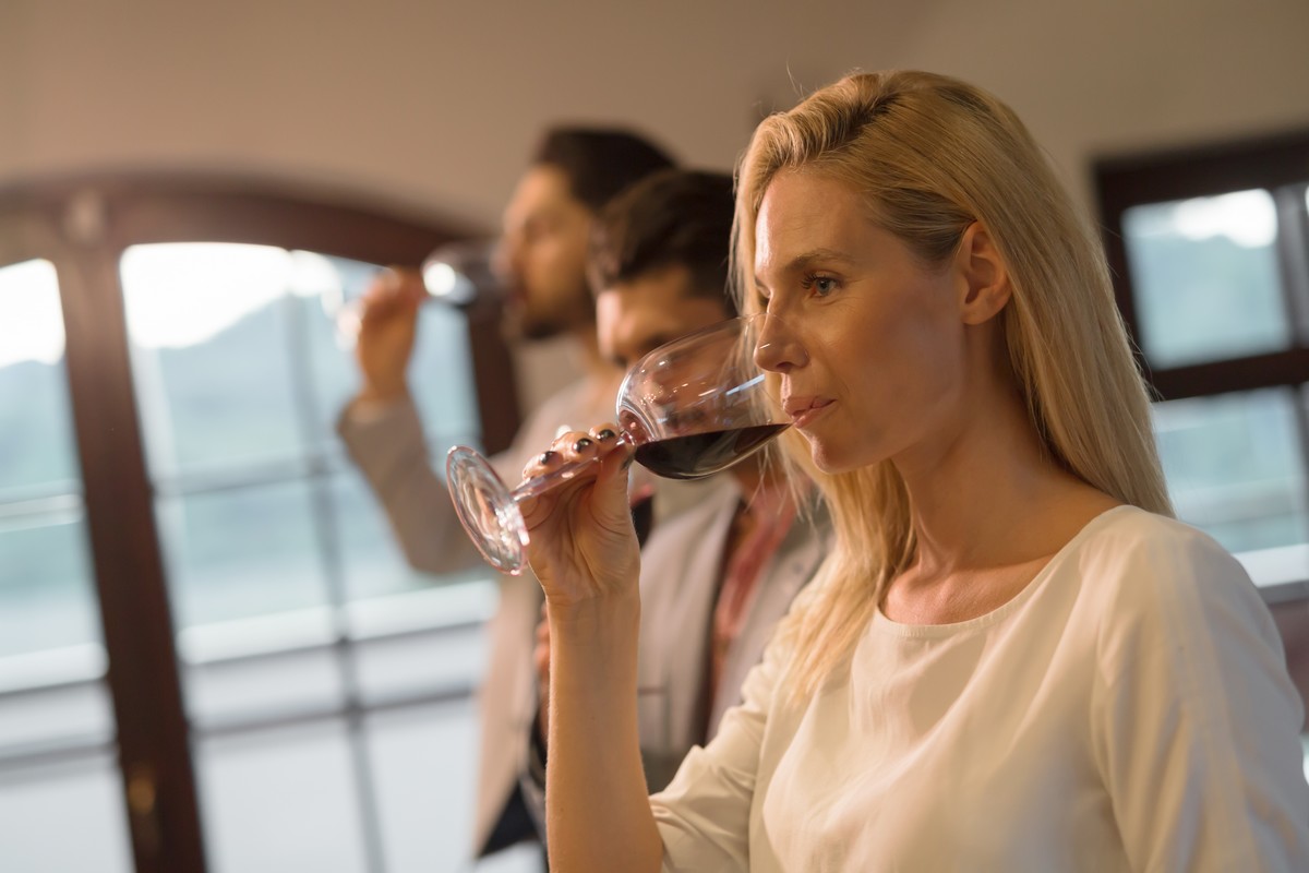 Elégante dame déguste du vin rouge, deux messieurs en arrière plan dégustent également