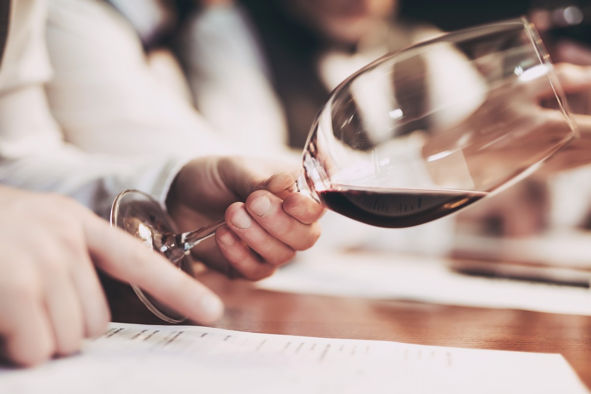 Main d'une personne qui incline son verre de vin rouge tout en lisant 