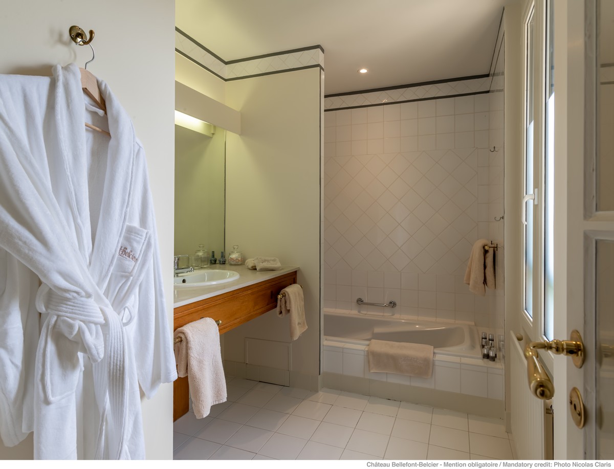 Peignoir blanc suspendu dans salles de bains verte et blanche, baignoire et vasques
