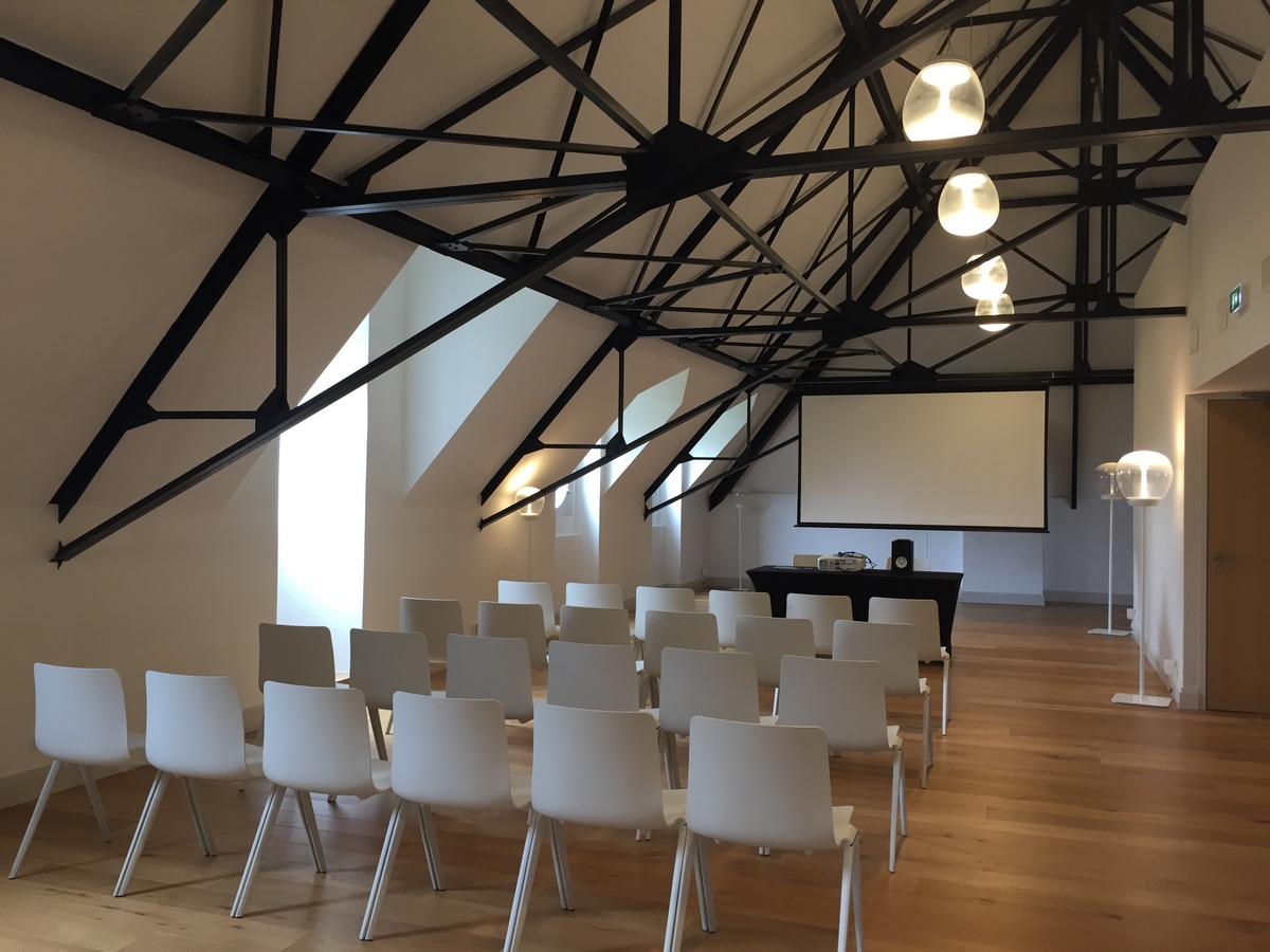 Petite salle de séminaire en théâtre, chaises, écran, poutre apparente noir en acier