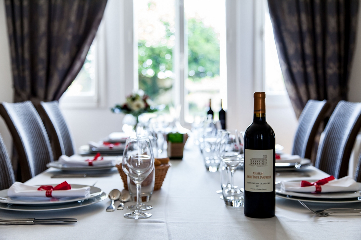 Table joliment décorée, bouteille de vin rouge, rideaux, assiettes avec noeud rouge