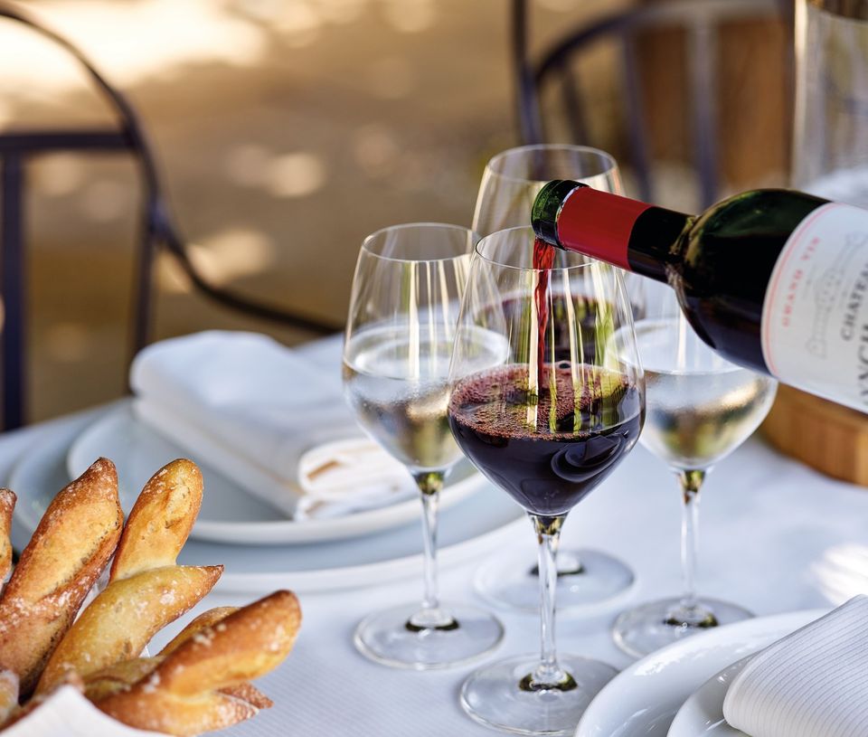 Table dressée restaurant avec service de vin rouge depuis la bouteille, baguettes de pain