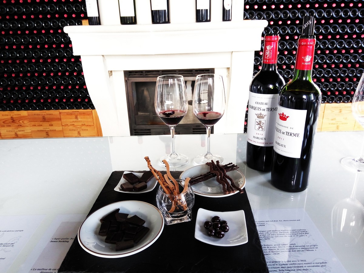 Chocolat, 2 bouteilles de vin rouge et 2 verres de vin rouge posés sur table blanche