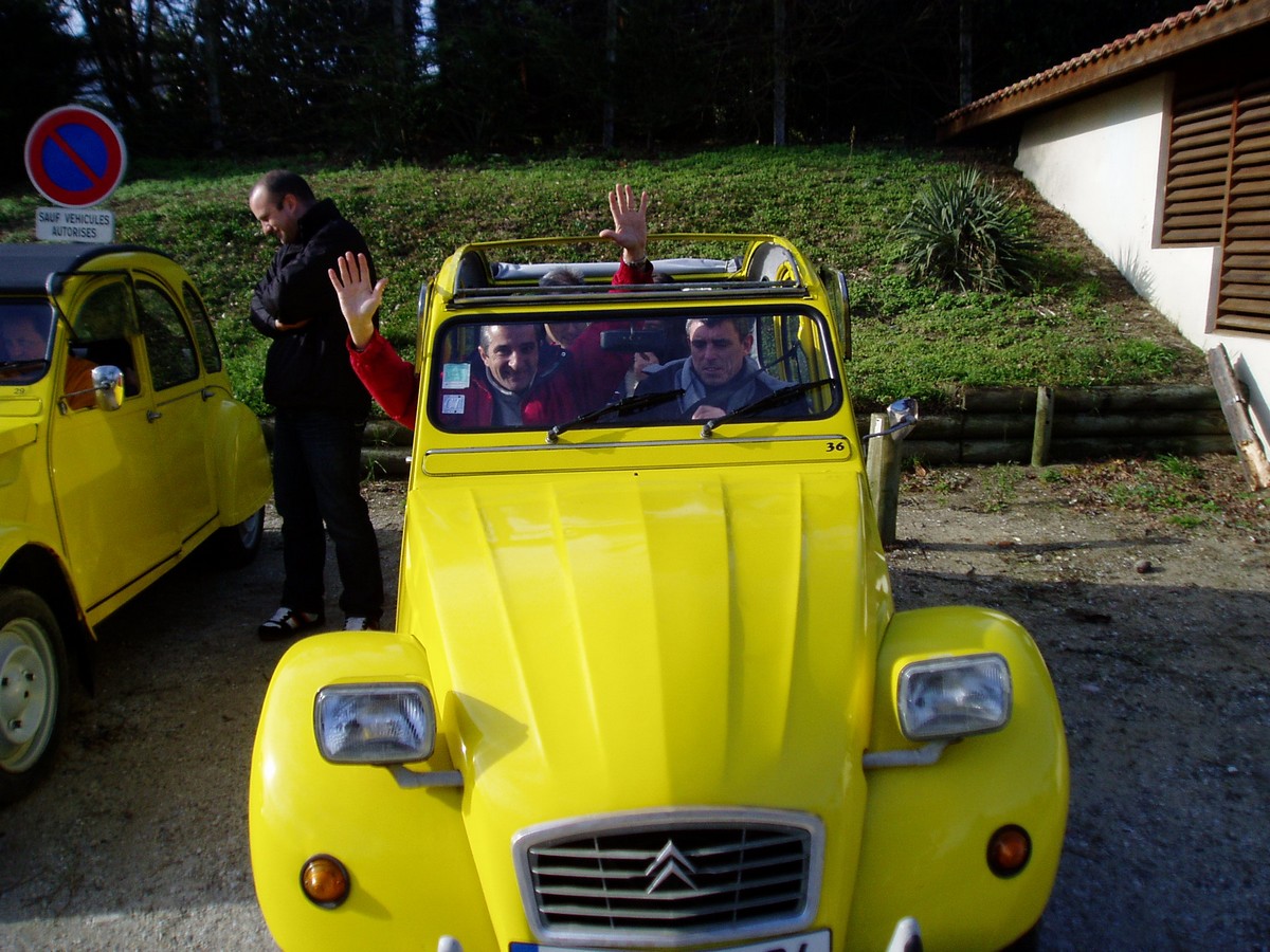 Dans une voiture 2cv décapotable jaune, des hommes lèvent les bras